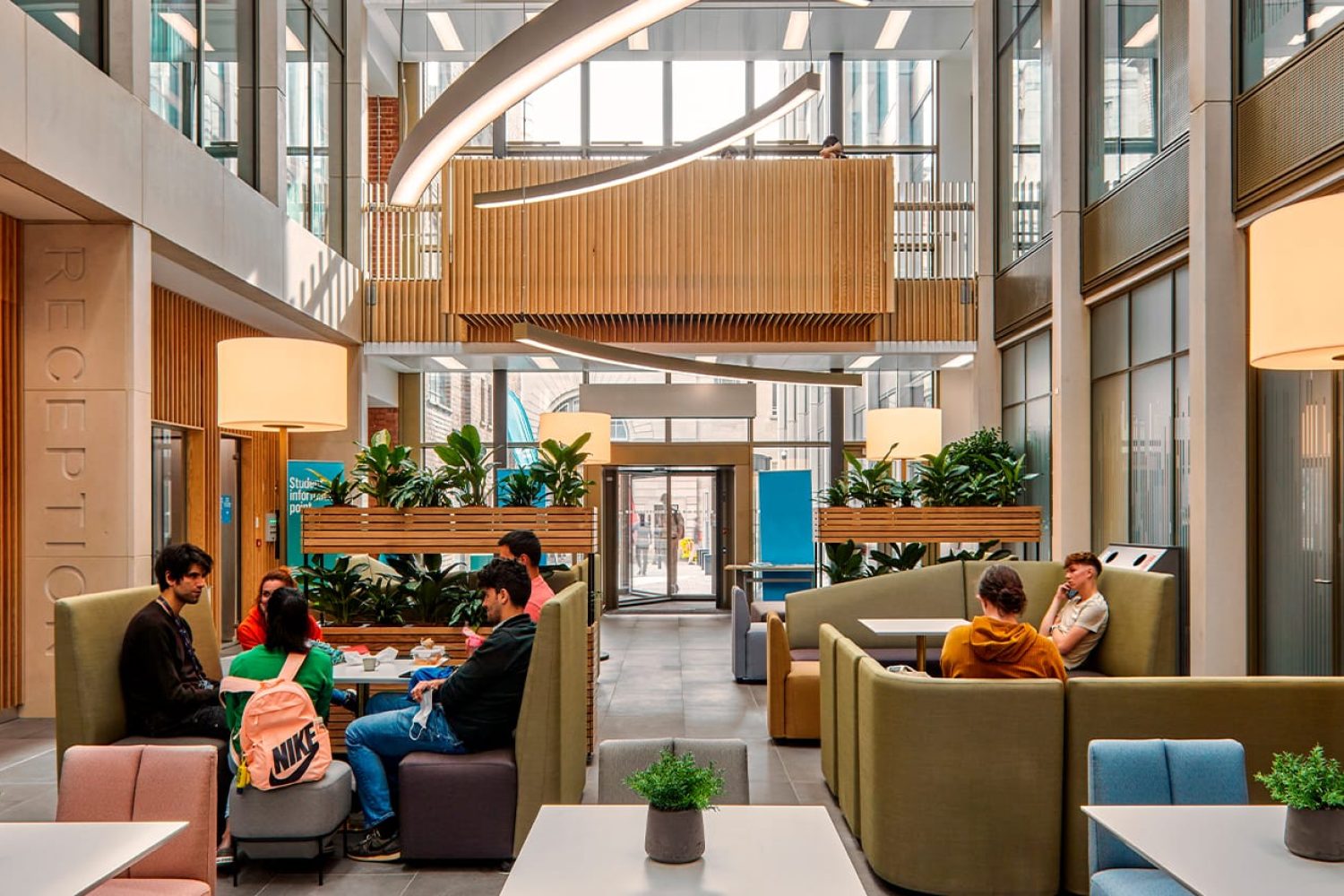 A group of people sitting at tables and on modular seating office sofas in a lobby.