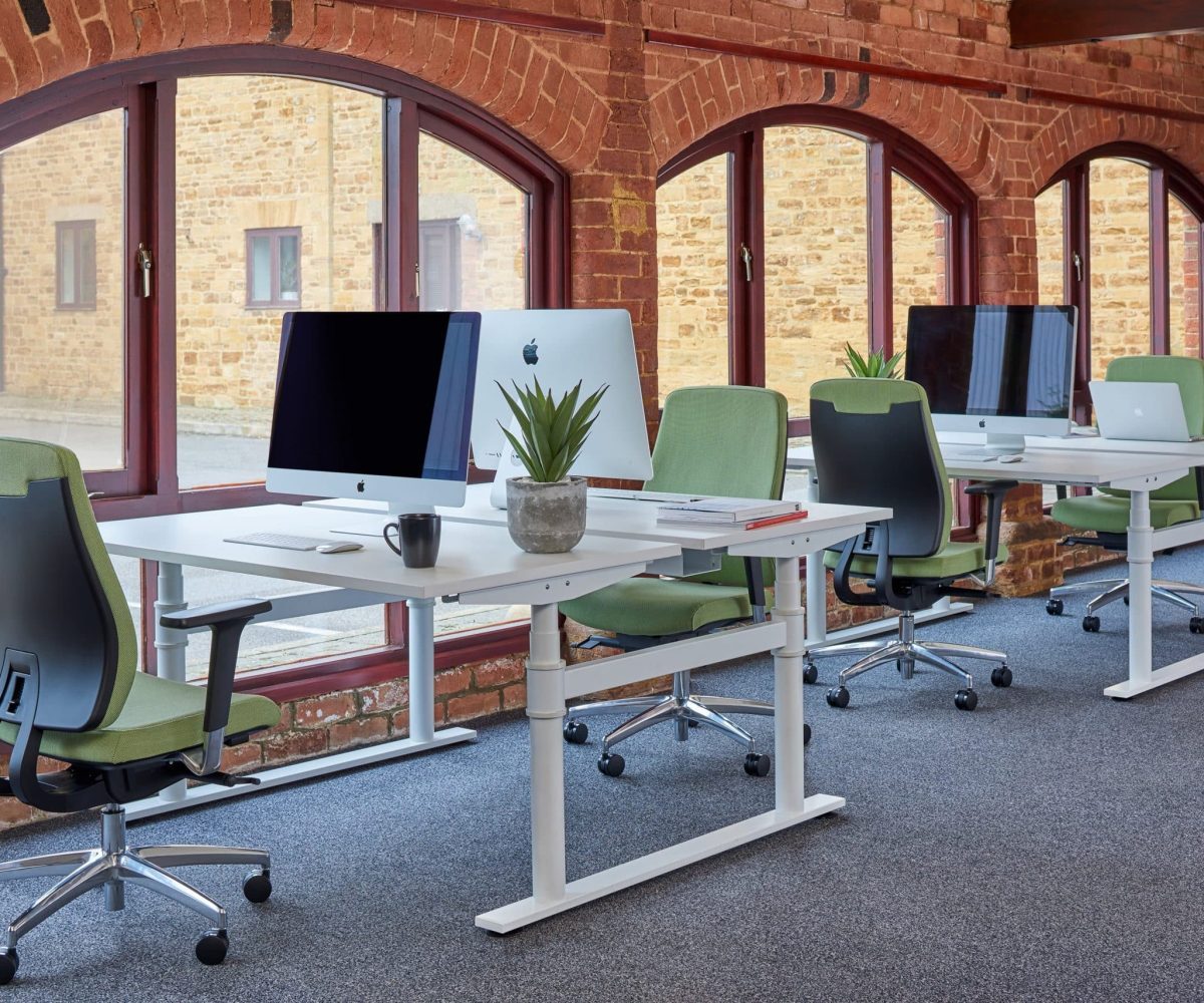 Office desk workstations in a brick building with green office desk chairs and monitors.