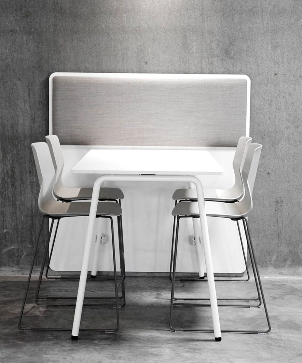 A white standing height table and office desk counter chairs in a concrete room.