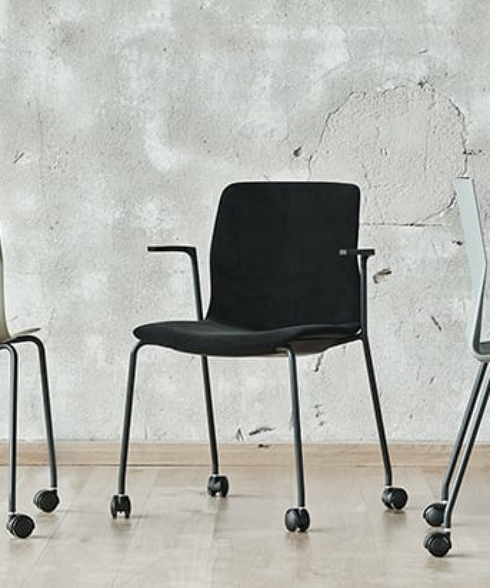Three chairs on wheels in front of a wall.