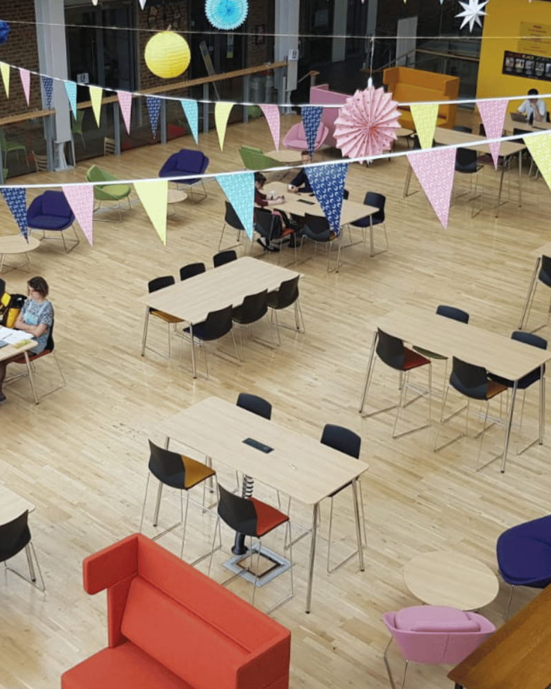A large open space with colourful tables and chairs and office seating.
