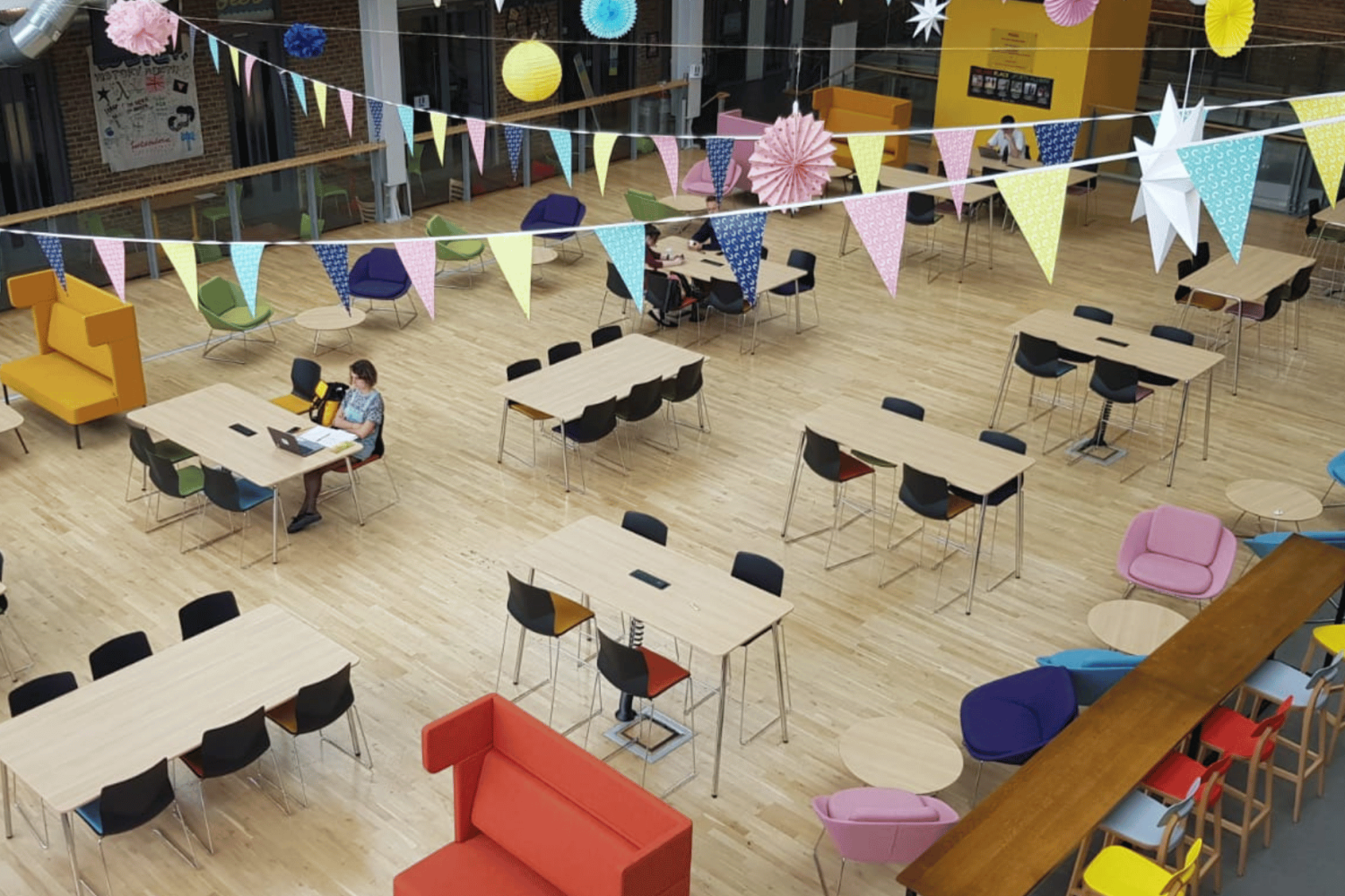 A large open space with colourful tables and chairs and office seating. 