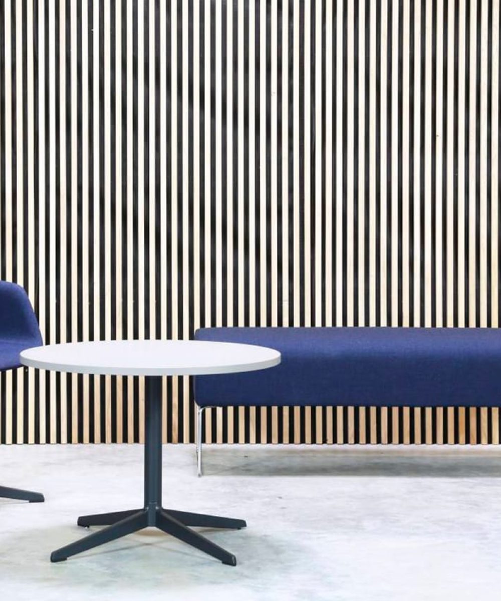 A blue chair, office bench and pedestal table in front of a wooden wall.